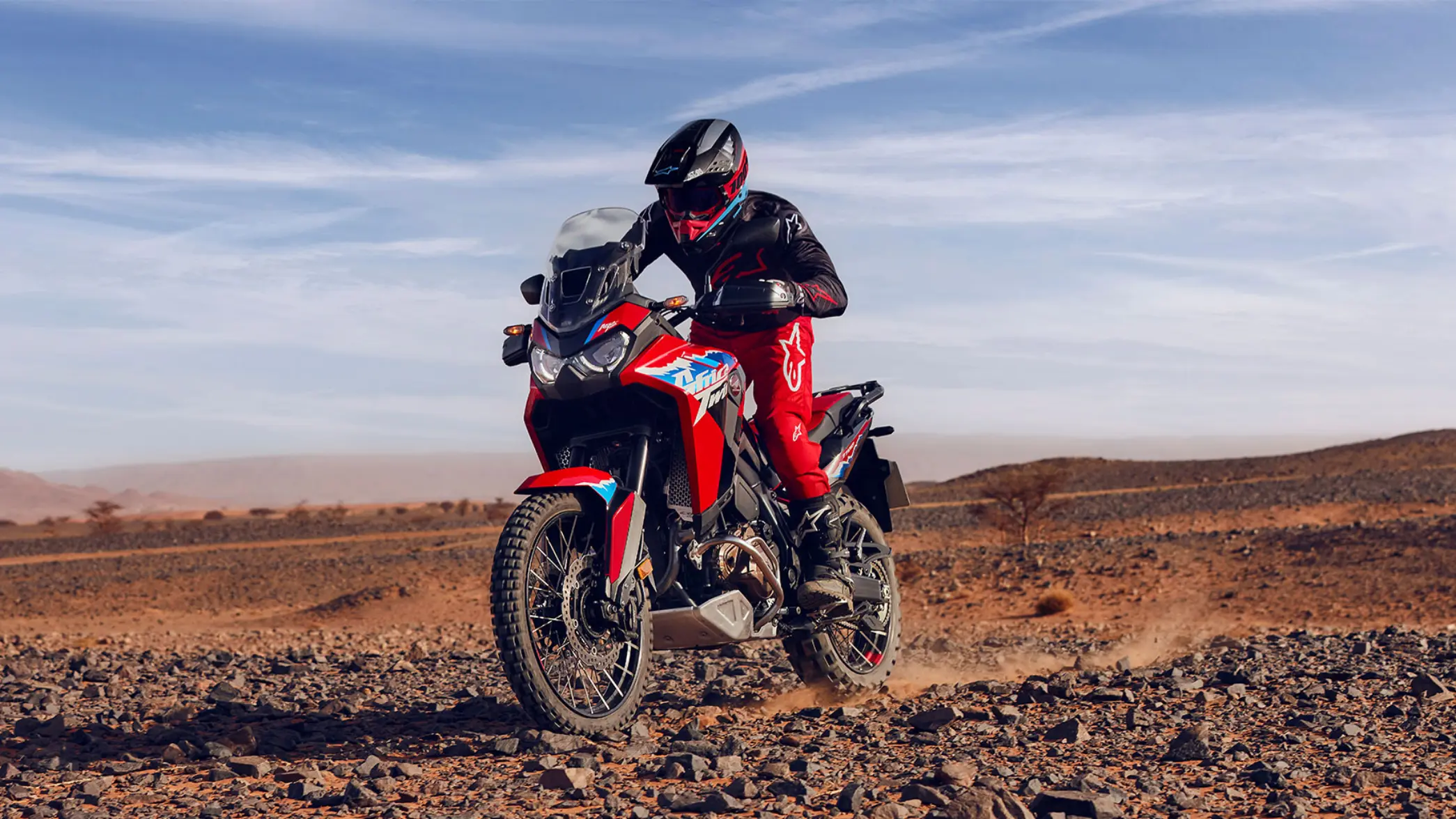 Fotómodell ül egy CRF1100L Africa Twin motorkerékpáron a sivatagban.